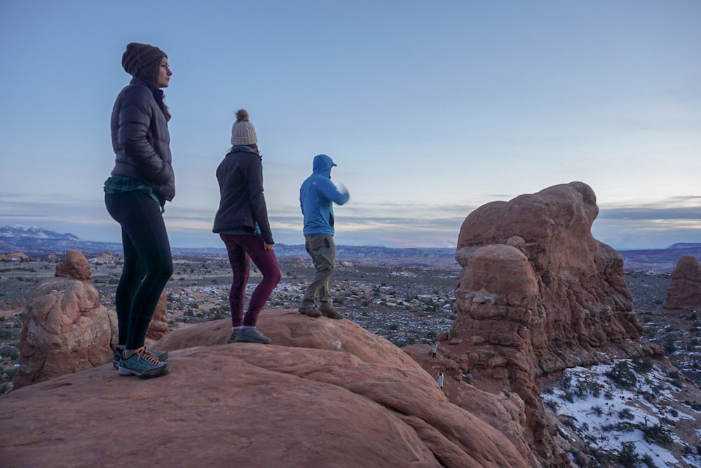 Three hikers admiring the view during their Arches National Park itinerary. 