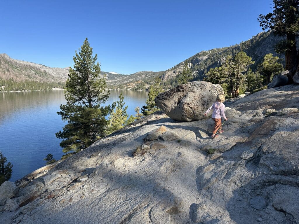 A girl hiking along a rocky shore of a mountain like near echo lakes, california.