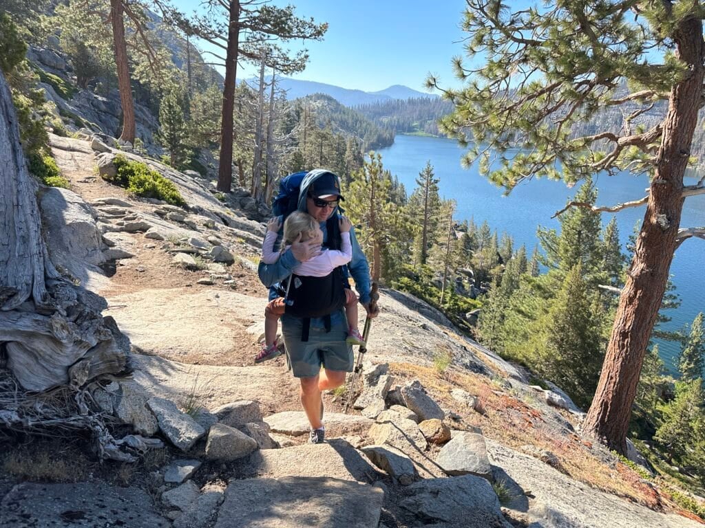 A dad and daughter are hiking in the mountains with blue lakes and pine trees.