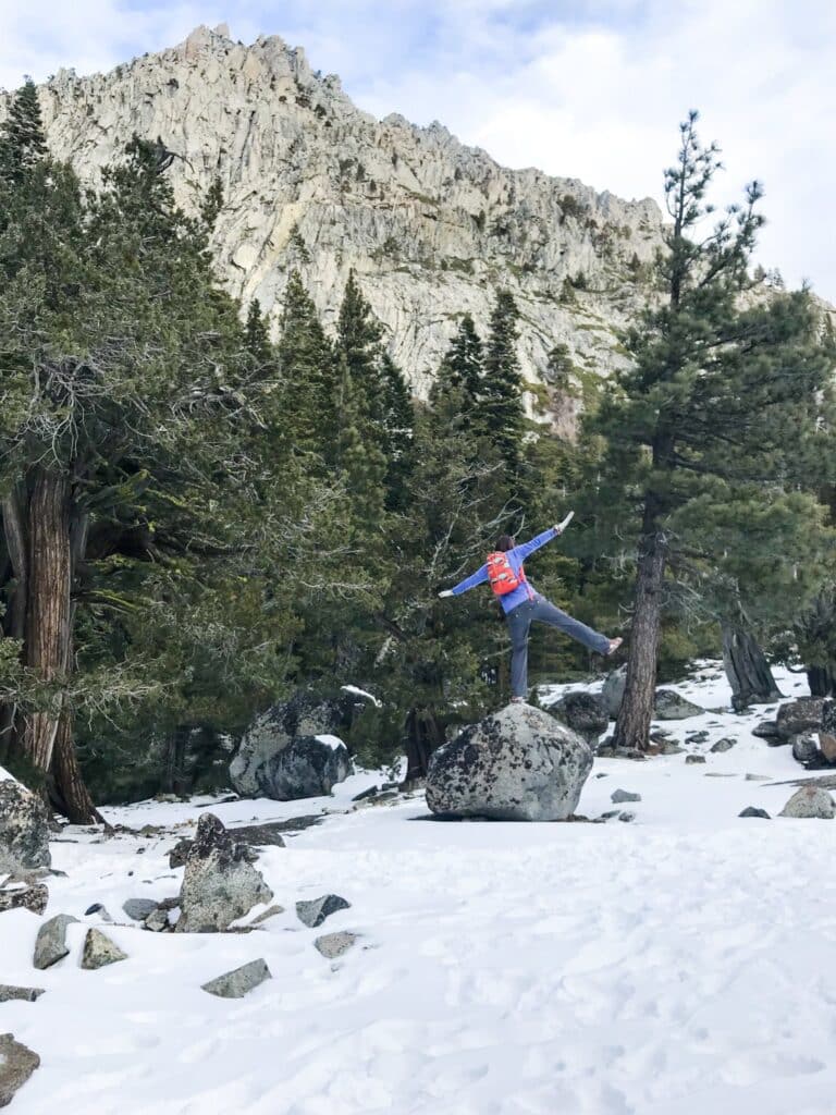 A person standing on a rock in the snow in the mountains with a big rocky mountain in the background