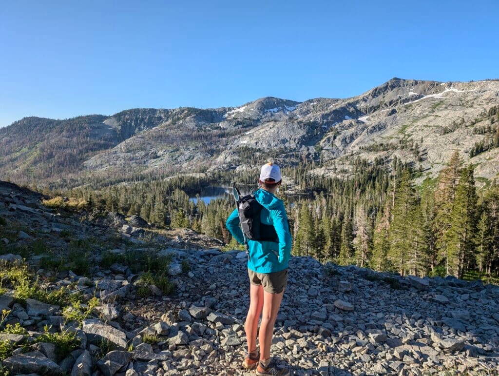 A woman trail running in the desolation wilderness near lake tahoe. Rocky mountain peaks and pine trees are in the background.
