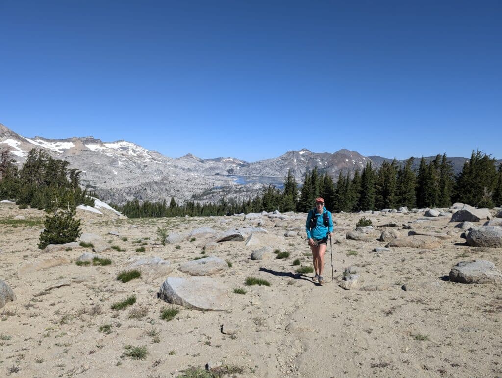 A woman trail running in the desolation wilderness with snow capped mountains in the distance.