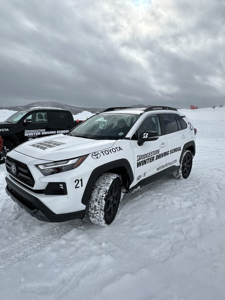 Attending the bridgestone winter driving school in steamboat springs is one of the top things to do in Colorado in winter. A white vehicle with a logo on it has snow-covered tires on a cloudy day.