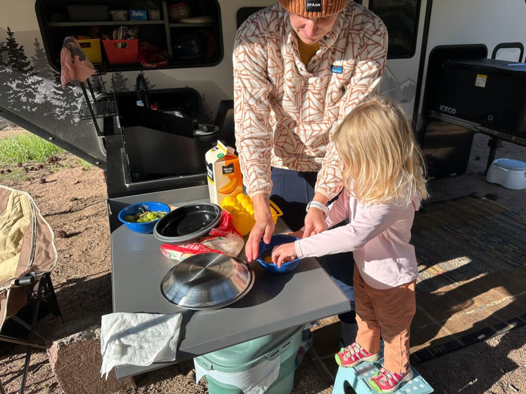 A mom and a toddler cracking eggs to cook while camping.