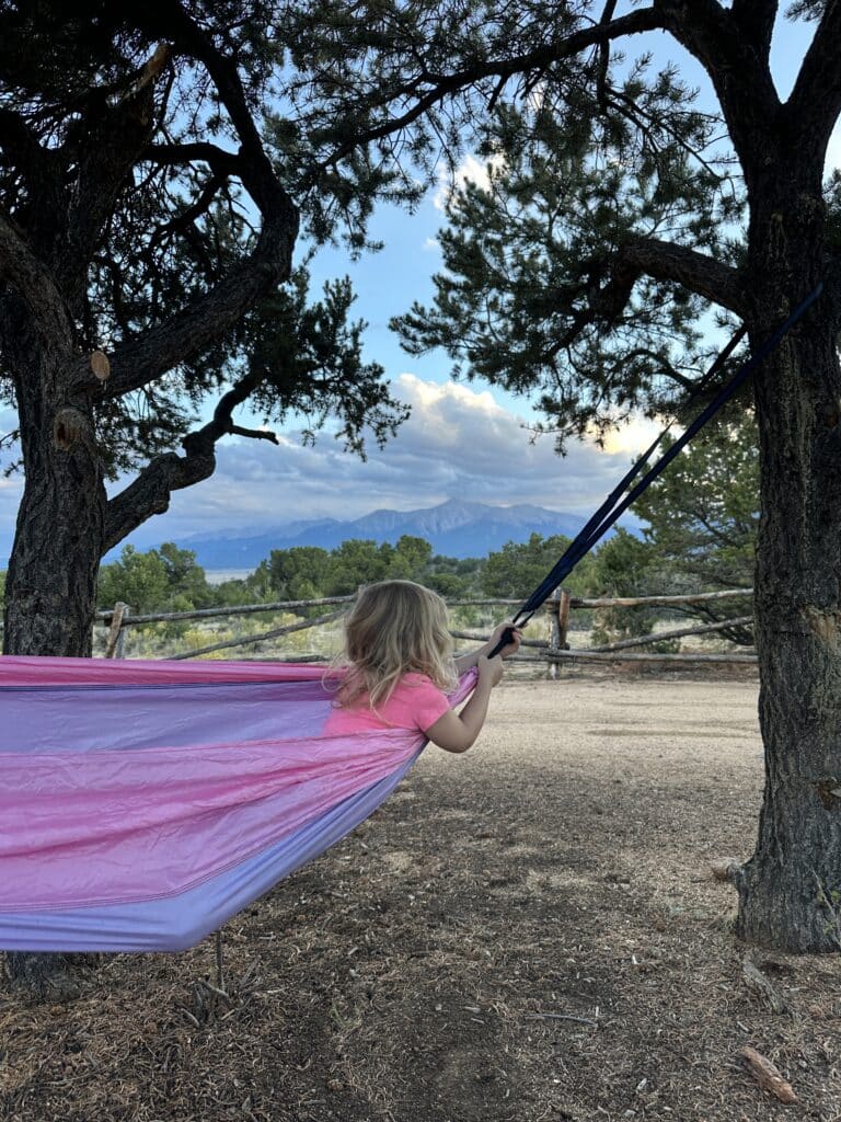 A toddler playing in a hammock at a mountain campsite.