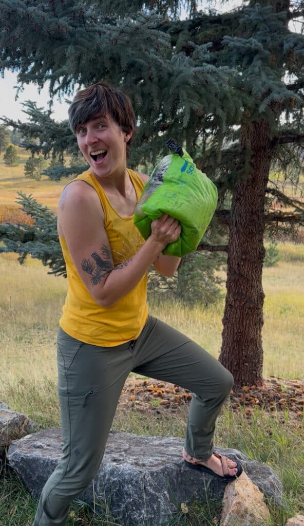 A persona using a portable washing machine bag called a Scrubba by shaking the bag and smiling.