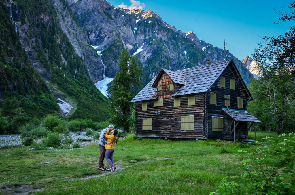 Couple kissing in front of a log cabin in Olympic National Park along the Enchanting Valley trail. 