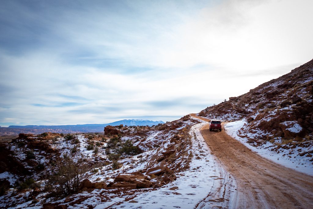 Jeep driving along Gemini Bridges with snow on the ground during one of the best Moab jeep tours of them all. 