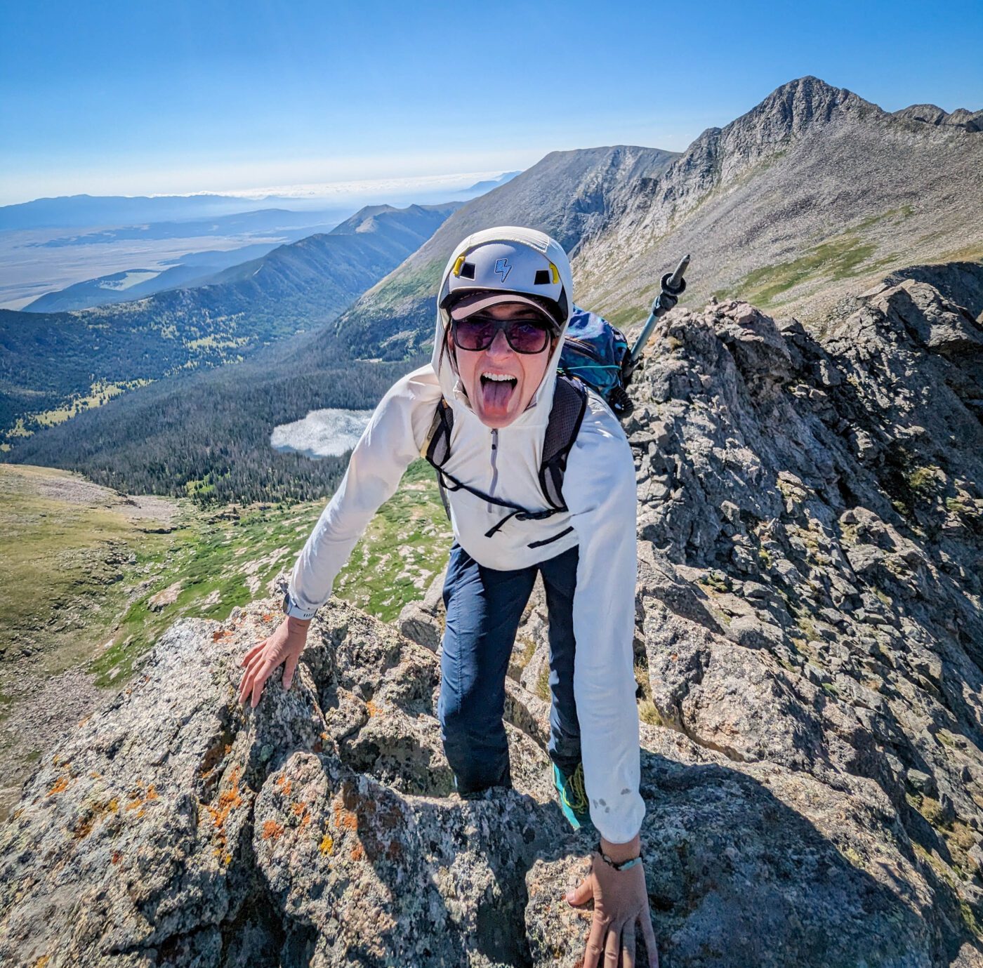 Meg hiking a mountain with a helmet on while wearing a white sweatshirt, black sunglasses, and a backpack.