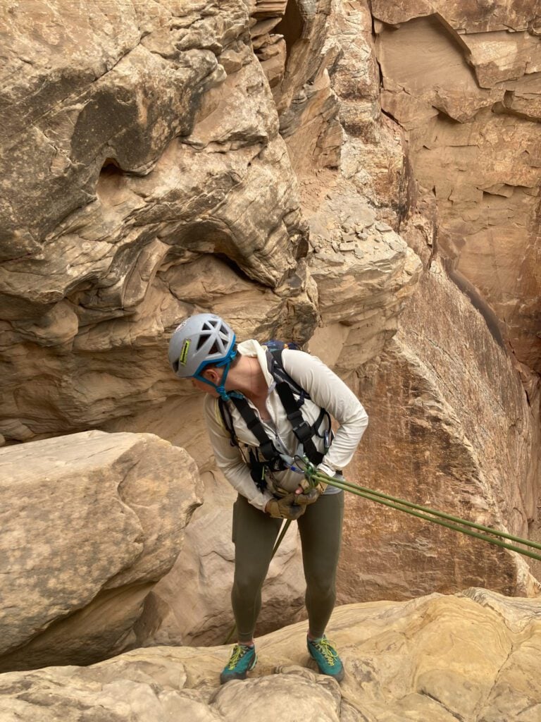 A pregnant person rapelling in a red rock slot canyon in the San Rafael Swell utah.