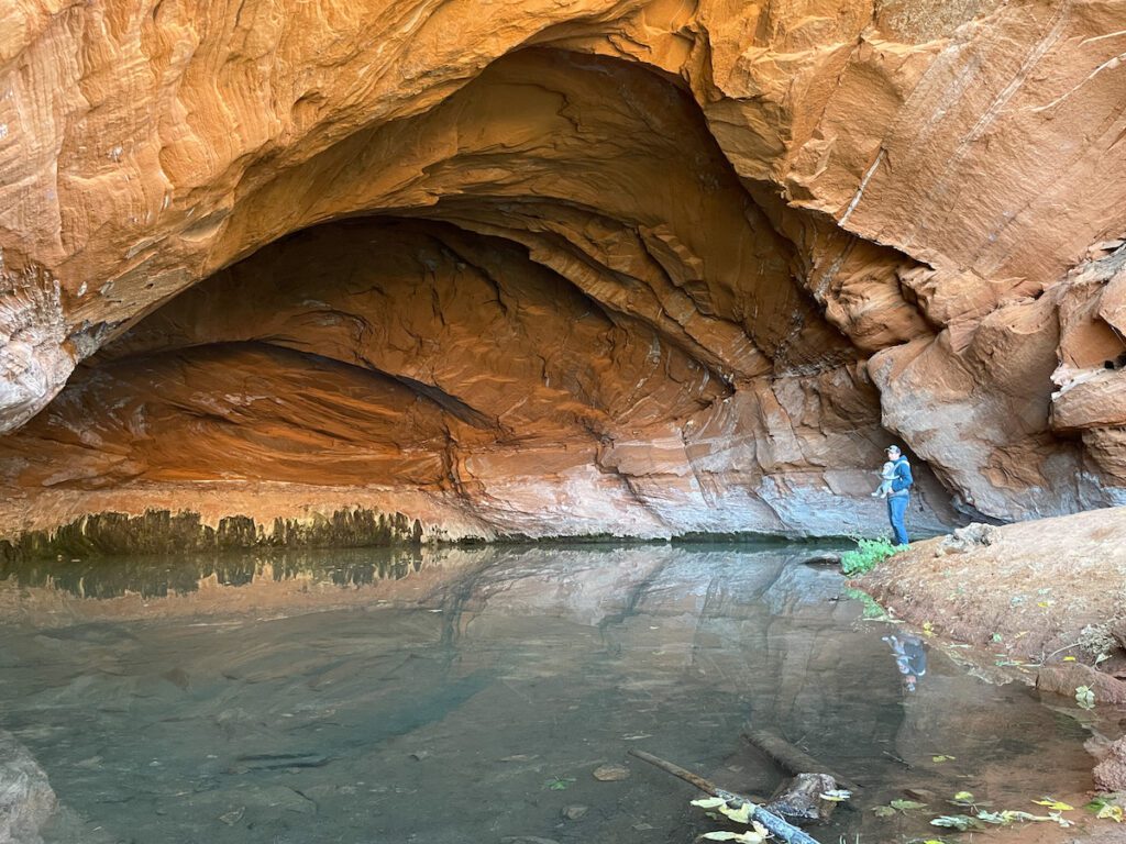 View of a person standing by the water near a sandstone cave in Kanab, Utah.