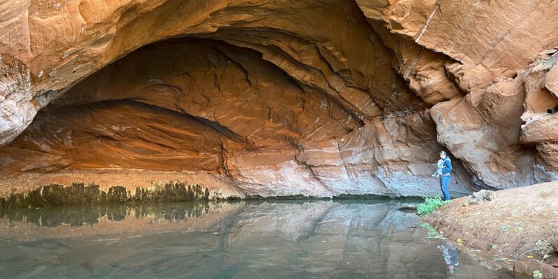 View of a person standing by the water near a sandstone cave in Kanab, Utah.