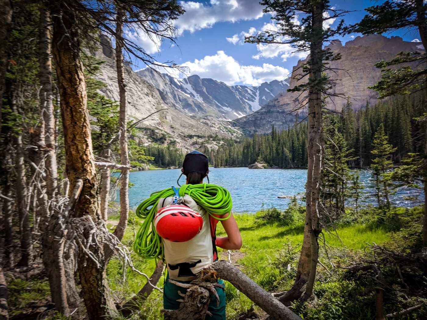 Meg is staring at an alpine lake in RMNP. She has a backpack on with green rope and a red helmet.