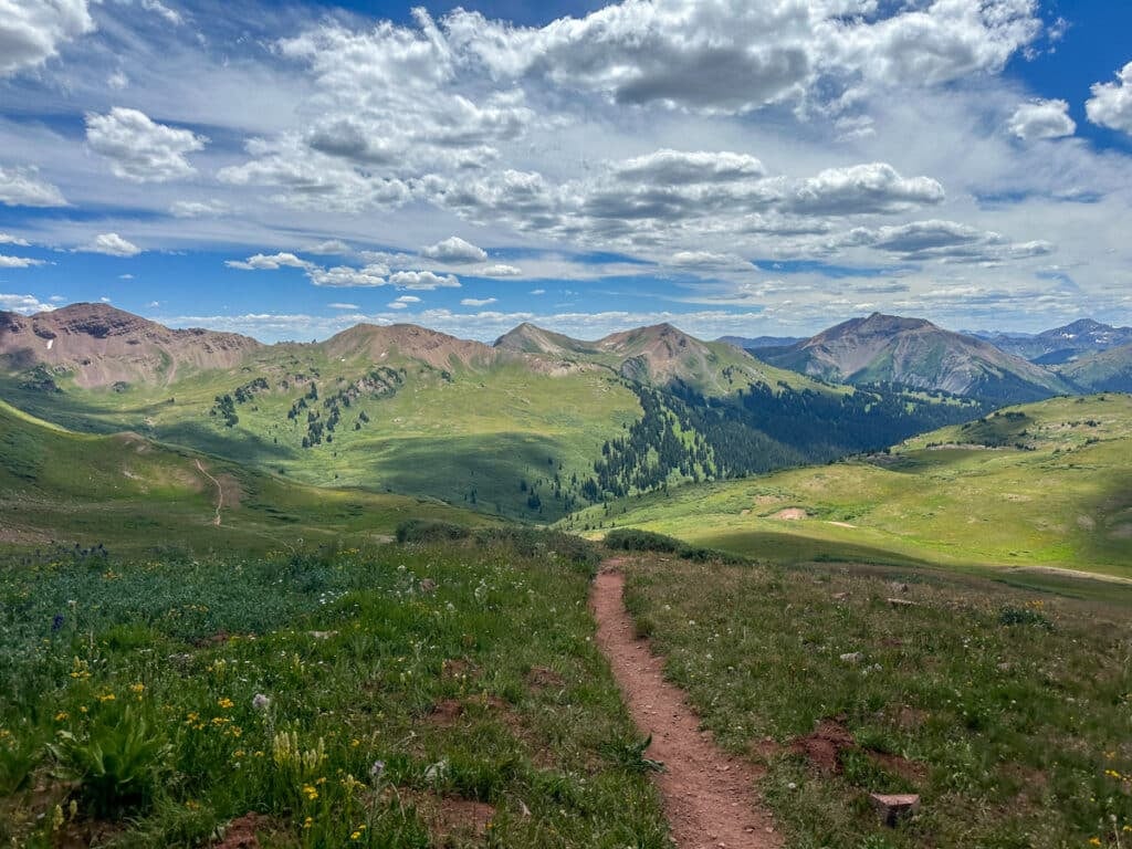 A trail winding through a lush mountain valley along the Four Passes Loop in Colorado