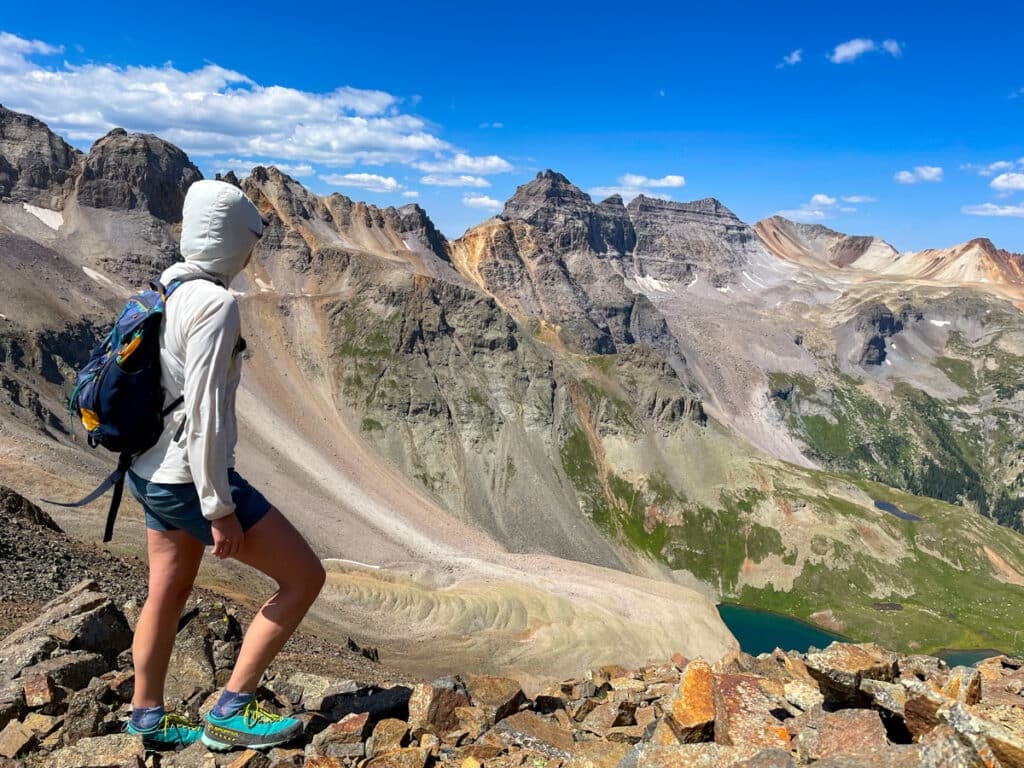 a woman standing on top of a mountain overlooking a rocky ridge with lakes below.