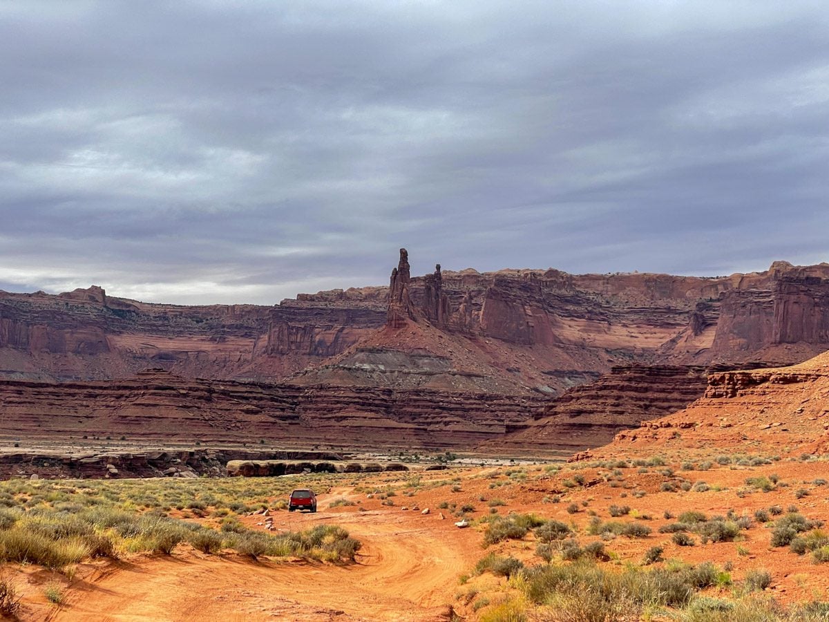 Two red rock towers in a canyon with the dirt White Rim road winding through it.