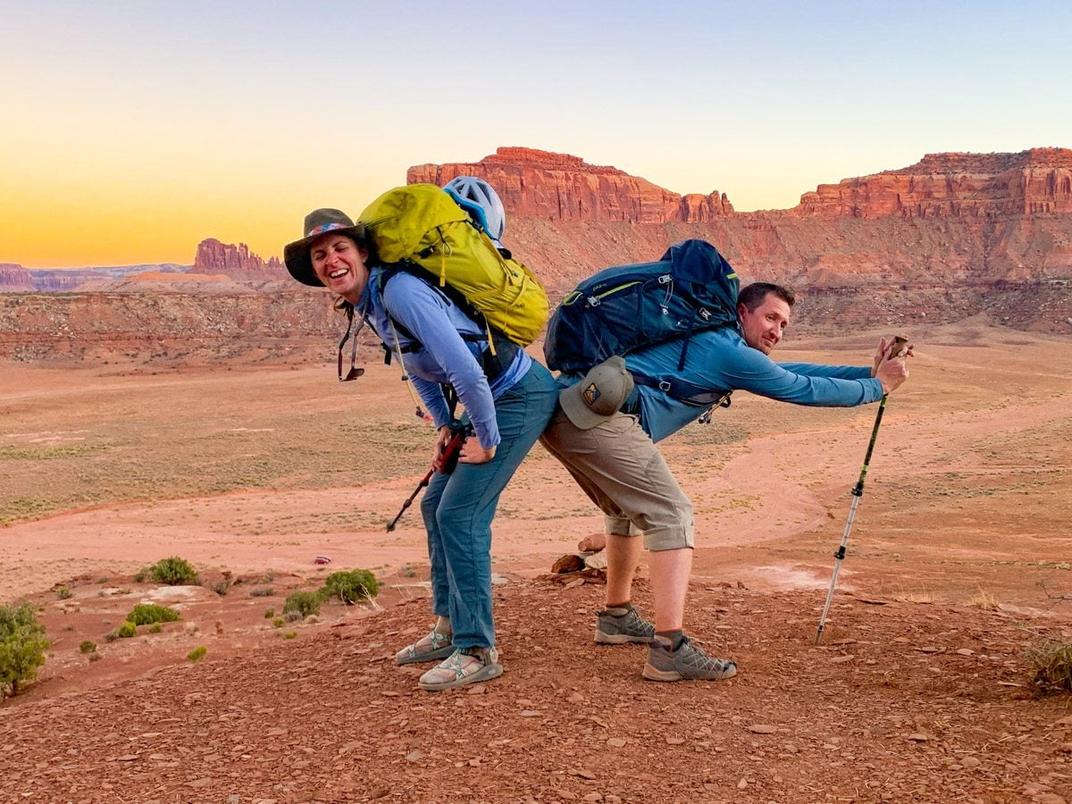 A man and woman posing in front of a cliff face at sunset at Indian Creek, Utah.