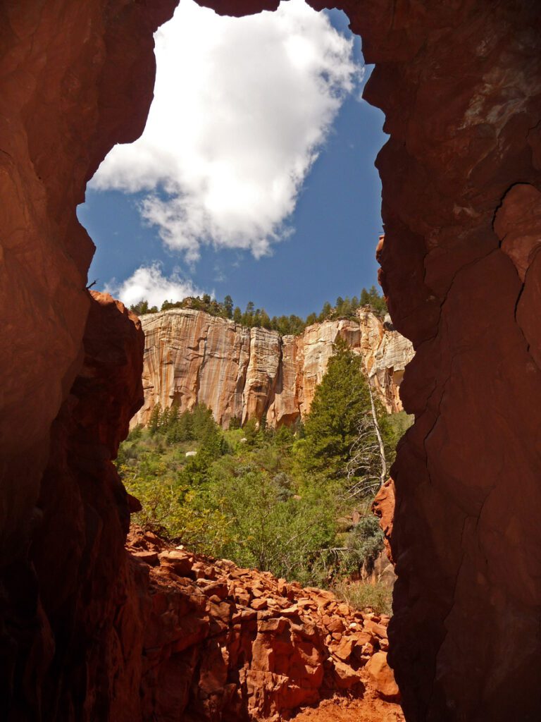 A view through the Supai Tunnel. It has tall walls along the canyon and a view of the desert landscape with trees and red rocks. 
