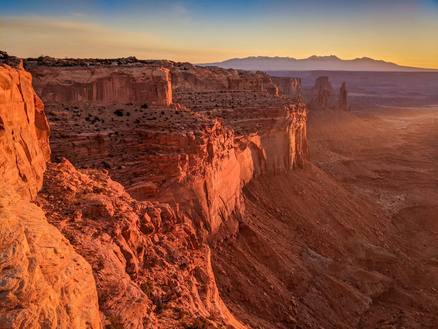 Sunlit red rock cliffs with mountains in the background in Canyonlands National Park near Moab.