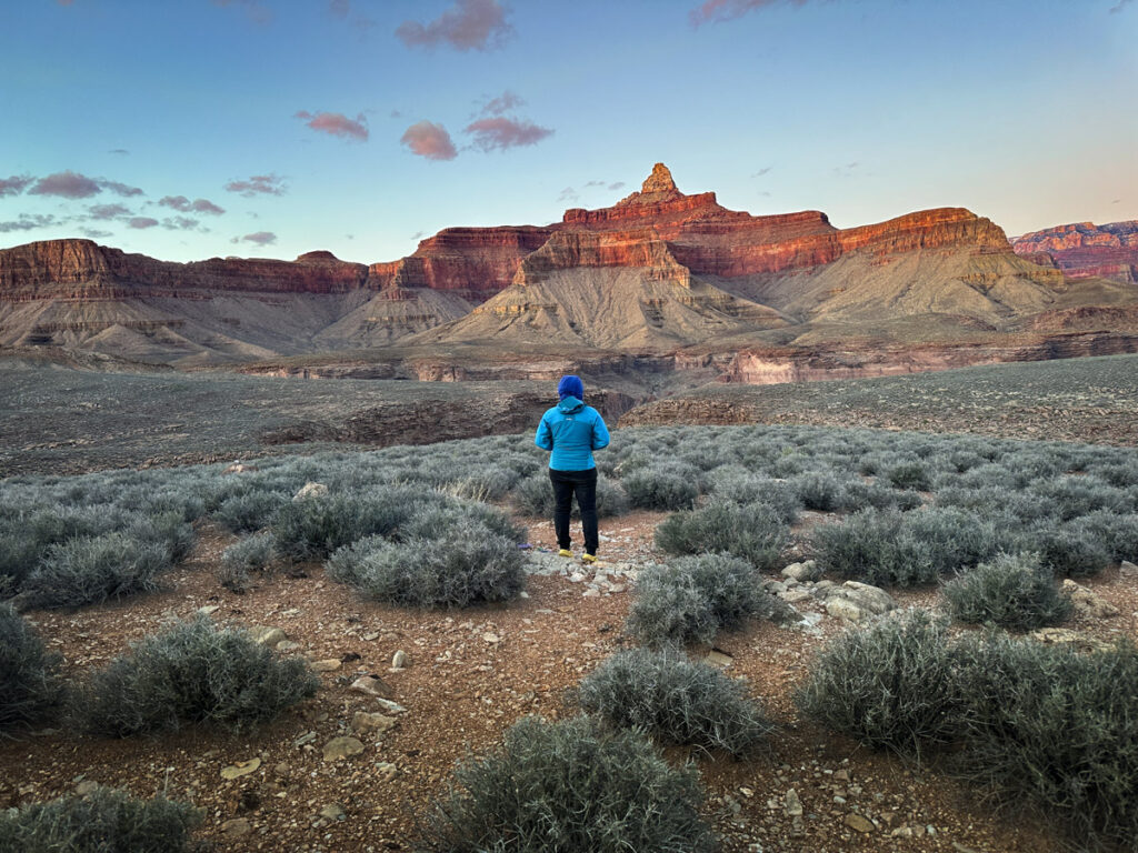 Grandview to bright angel backpacking in march. A woman standing at sunset in the desert landscape of the grand canyon with a towering red rock mountain.