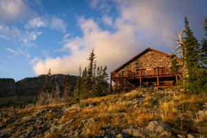 A wooden building sitting on the side of a mountain at sunset in Granite Park. The skies are blue and filled with clouds.