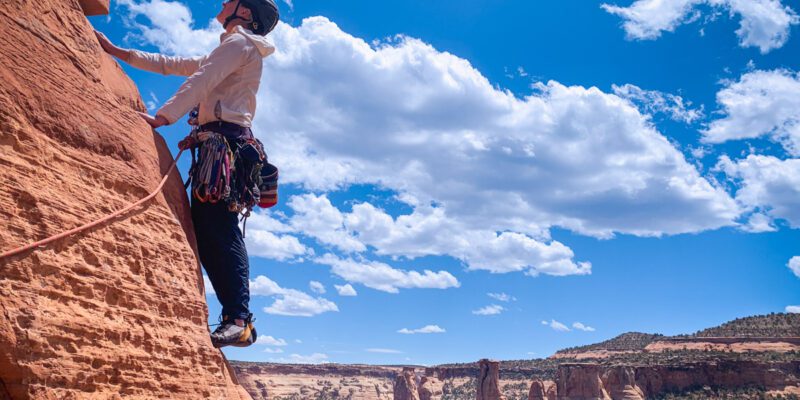 Meg is climbing the face of a mountain in Colorado National Monument on a sunny day.