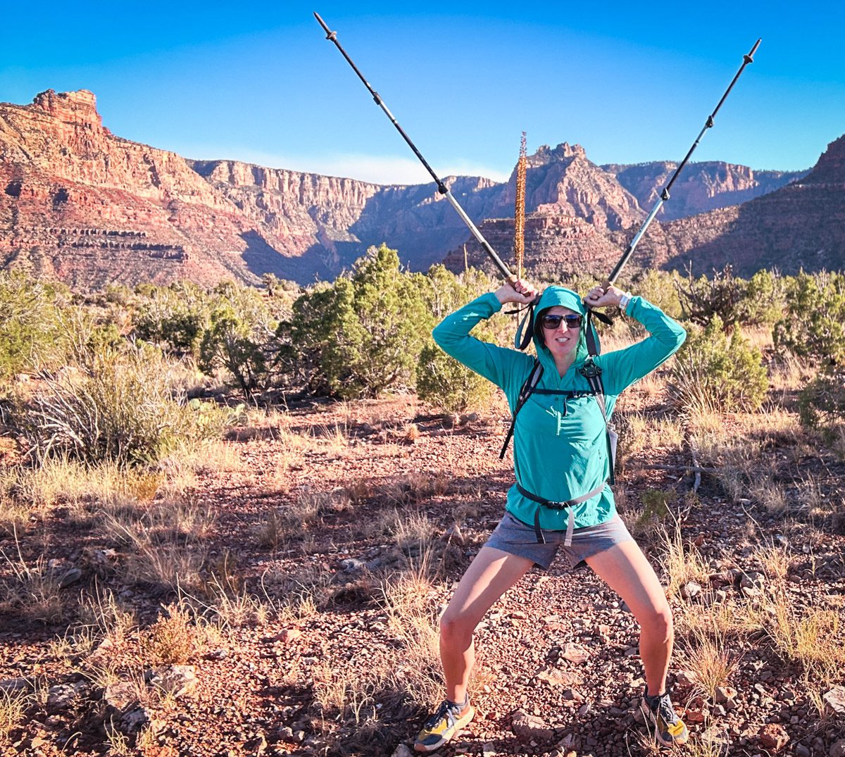 A woman wearing a sunshirt standing with hiking poles on her head in a red rock canyon.