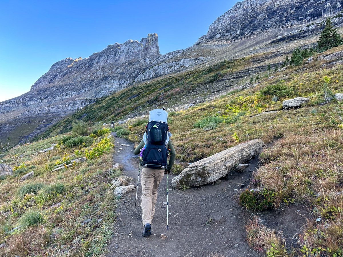 A man walking with a baby on his back in the mountains of Glacier National Park.