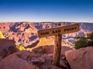 A view of a wooden sign that says, "Ohh Ahh Point" sitting in front of the Grand Canyon during sunrise.