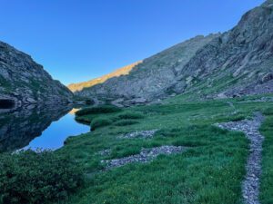 View of the a green valley with a lake and mountains at the Crestone Traverse.