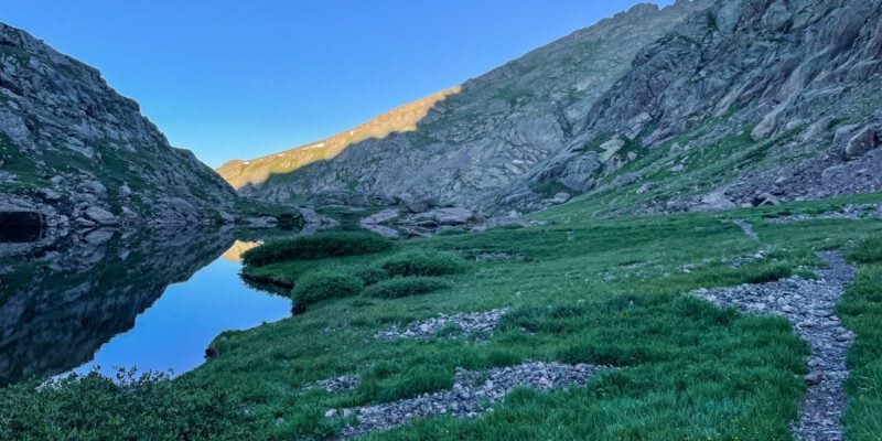 View of the a green valley with a lake and mountains at the Crestone Traverse.