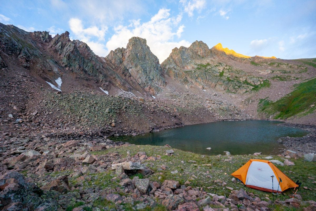 a backpacking tent set up near a lake in the mountains at sunset.