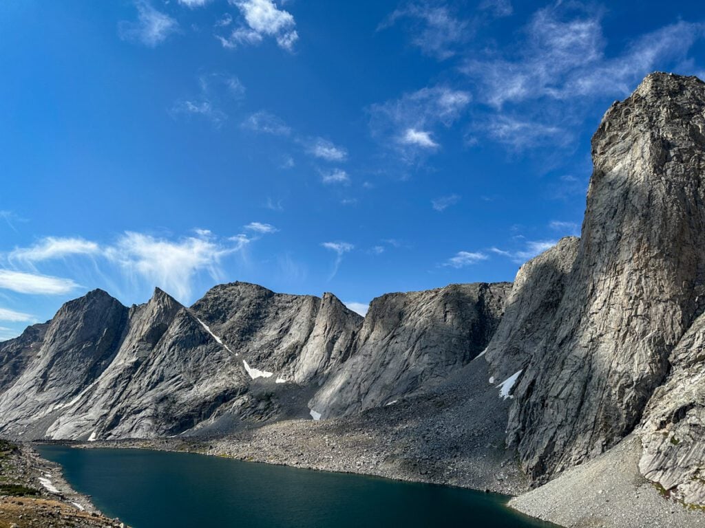 A dramatic mountain peak on a sunny day with a large alpine lake at the base.