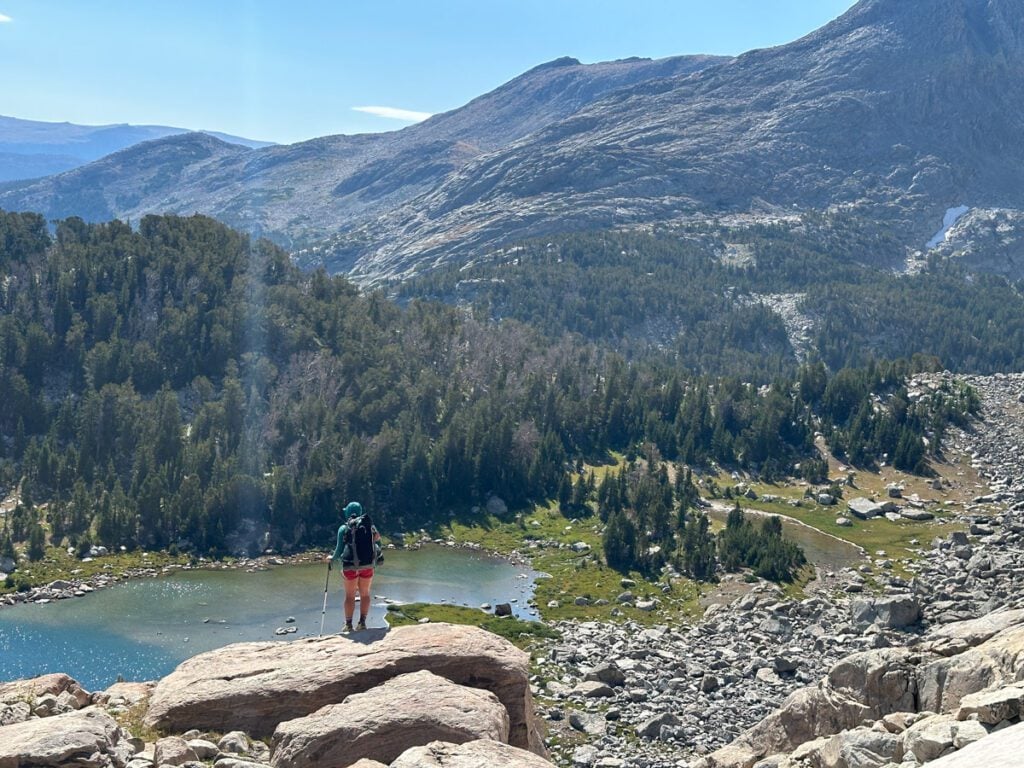 A woman standing on a rock looking for a way to descend into Camp Lake - a high alpine lake in Wyoming.