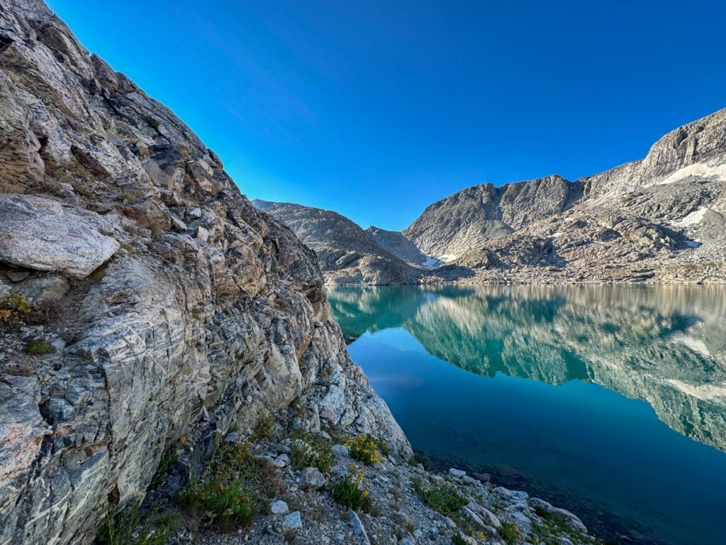 A still alpine lake surrounded by cliffs that cascade into the water.
