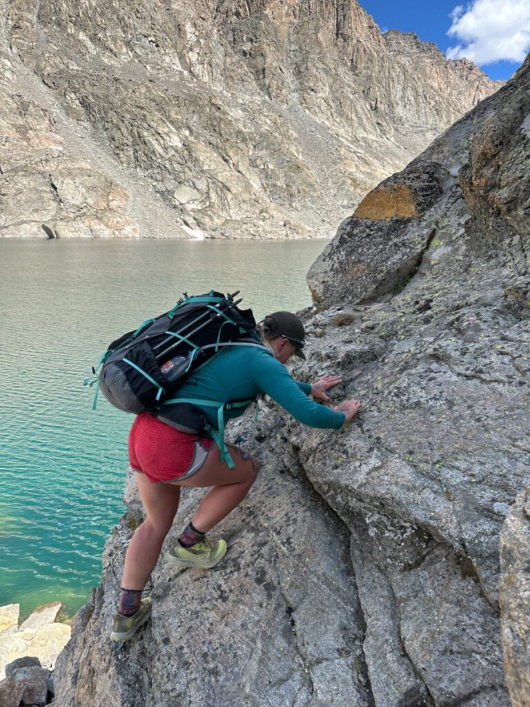 A woman scrambling up rocks in the alpine lakes basin on the wind river high route.