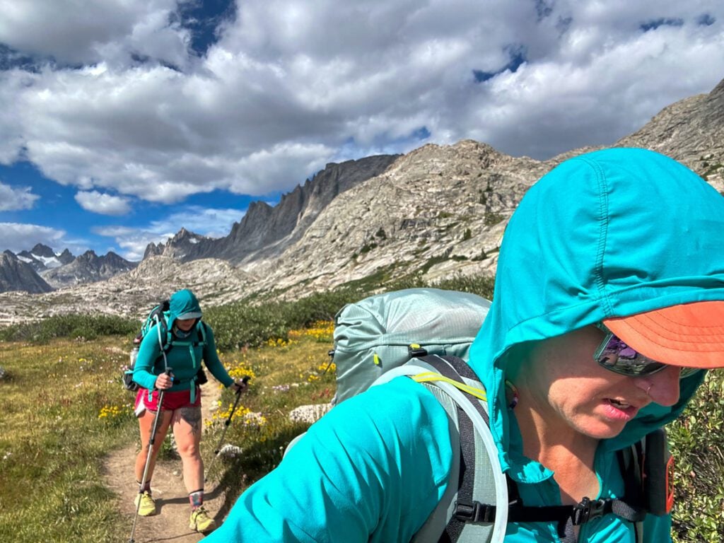 Two women walking on a mountain trail during a sunny day.