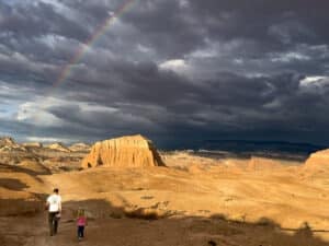 A dad and daughter hiking under a rainbow in Cathedral Valley