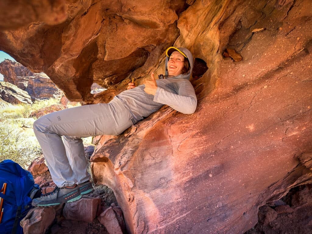 A woman sitting awkwardly under an overhanging rock.