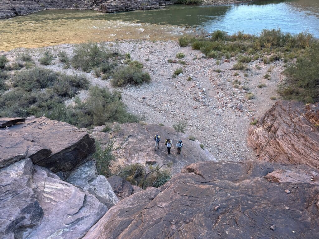 People standing at the base of a cliff in the Grand CAnyon.