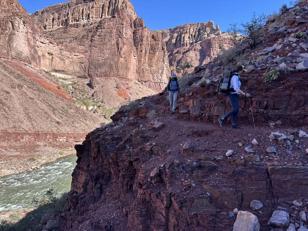 hikers along the escalante route of the grand canyon with the colorado river in the background