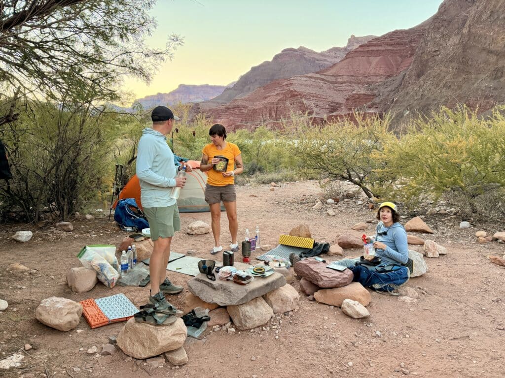 Three people eating dinner on a rock at Tanner Beach in the Grand CAnyon