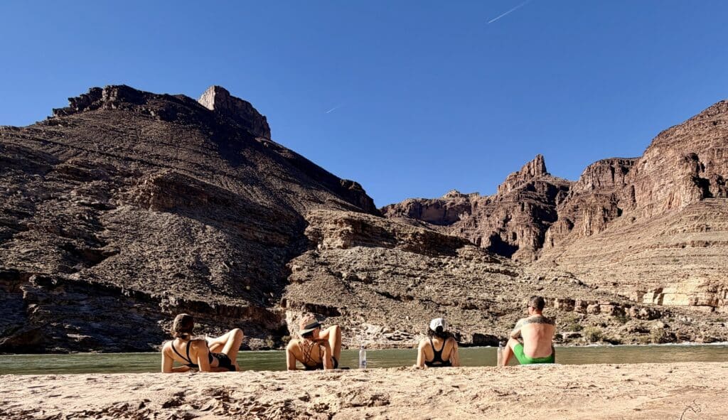Four people sitting next to a soft sand Escalante Beach at the Grand Canyon