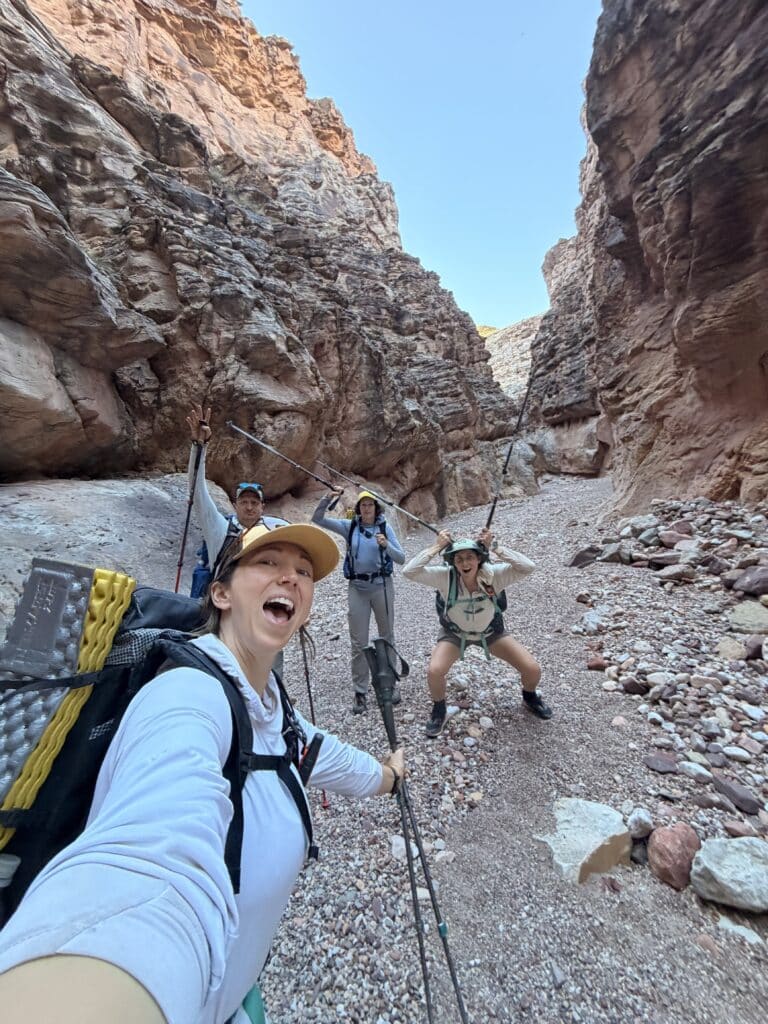 Three women hikers in a slot canyon with hiking poles along the Escalante Route.