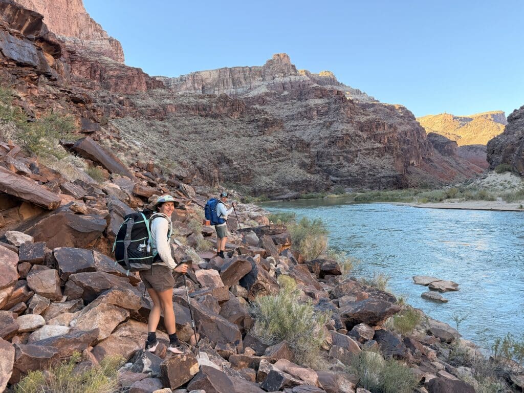 two people scrambling over rocks along the shores of the Colorado river in the Escalante Route.